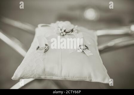 Deux anneaux de mariage reposent sur un coussin en soie brodé sur une table en verre transparent. Banque D'Images