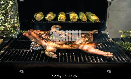 Le porc rôti croustillant qui est grillé au barbecue avec du maïs sur l'épi. Gros plan de délicieux cochon entier sur barbecue, cuisine maison. Chef Banque D'Images