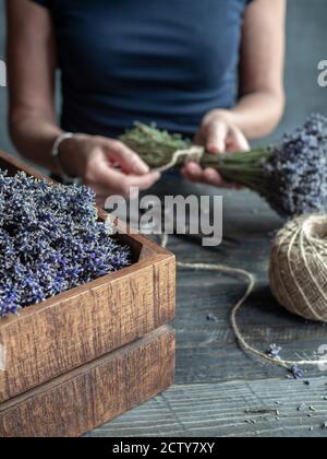 Les fleuristes en T-shirt bleu ont attaché un bouquet de lavande par ficelle. Table de travail avec laveurs, vieux ciseaux et une queue de ficelle de chanvre. Banque D'Images
