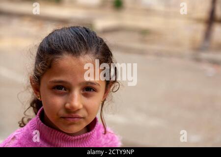 Tartus, Syrie 03/27/2010: Portrait en gros plan d'une fille syrienne brune de 8 ans dans un quartier pauvre de Tartus. Elle a une vieille traction rose déchirée Banque D'Images