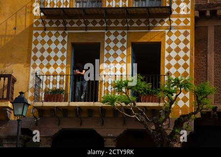 Vue sur un balcon élégant dans un appartement résidentiel vintage à la façade vibrante. Il y a un jeune homme qui se tient sur le balcon et qui penche au-dessus de la rambarde Banque D'Images