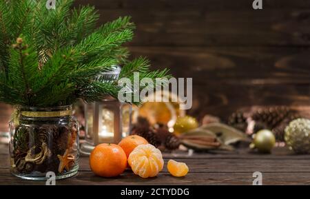 Concept de vacances de Noël ou de nouvel an. Composition de mandarines, brindilles de sapin avec cônes dans un pot en verre et décorations de vacances sur une table rustique en bois. Banque D'Images