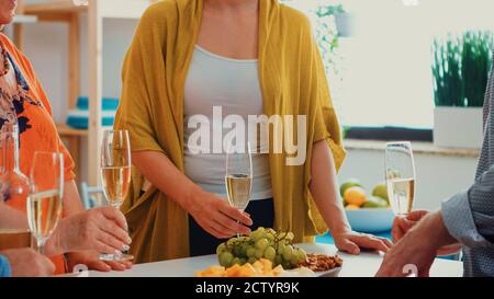Bonne famille en dégustant un verre de champagne. Les gens de deux générations parlent, assis autour de la table pour faire du toaster et célébrer un événement en buvant un verre de vin blanc. Banque D'Images