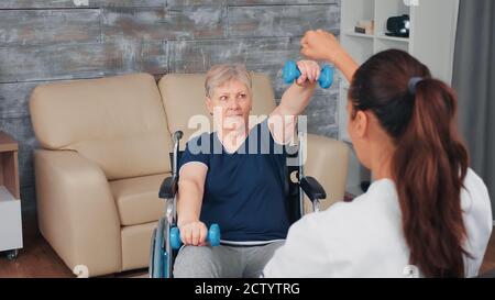 Femme âgée en fauteuil roulant qui fait de la formation en réadaptation à domicile avec un médecin. Personne handicapée handicapée aide professionnelle de récupération infirmière, soins infirmiers à domicile de retraite et de réadaptation Banque D'Images