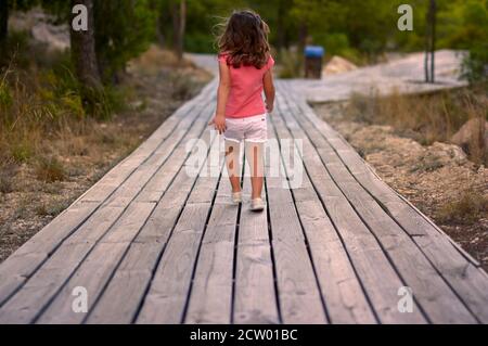 vue sur une petite fille qui marche sur une passerelle en bois le milieu de la forêt Banque D'Images