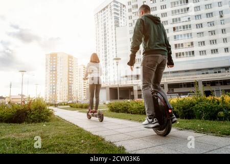 Jeune homme à cheval sur un monocycle et jeune femme en tenue décontractée en voiture sur un scooter électrique dans la rue de la ville Banque D'Images