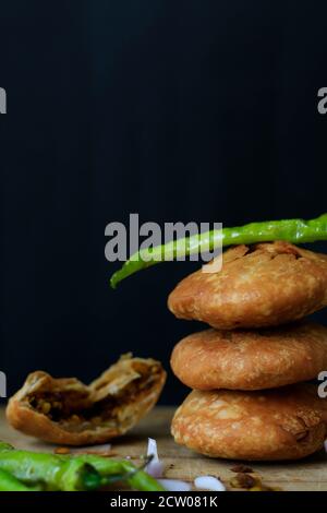 Délicieux en-cas indien kachori empilés les uns sur les autres et servis avec des piments verts et des oignons avec un fond noir de gros plan. Banque D'Images