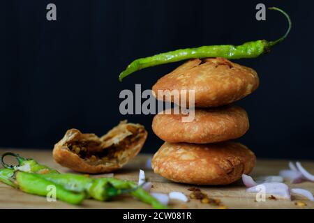 Délicieux en-cas indien kachori empilés les uns sur les autres et servis avec des piments verts et des oignons avec un fond noir sur une assiette en bois. Banque D'Images