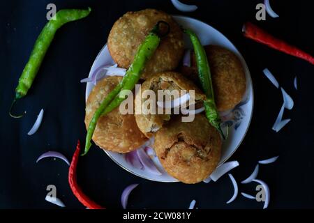 Délicieux en-cas indien kachori empilés les uns sur les autres et servis avec des piments verts et des oignons avec un fond noir de haut angle. Banque D'Images