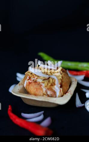 Chat kachori frit à l'indienne, recouvert de caillé et de sev et d'oignons sur fond noir avec des piments verts et rouges. Banque D'Images