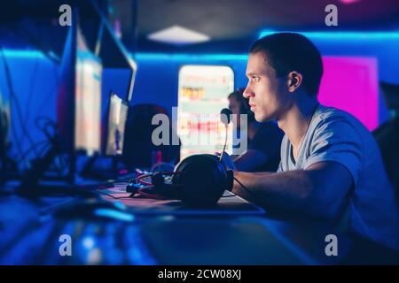 Cyber gamer professionnel jouant aux tournois en ligne ordinateur avec casque, rouge flou et fond bleu Banque D'Images