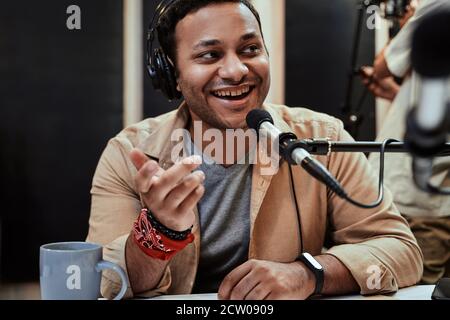 Portrait d'un jeune homme heureux animateur radio dans un casque souriant de côté pendant la conversation, la diffusion en studio Banque D'Images