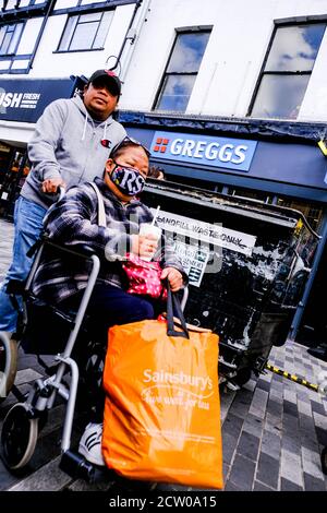 Homme poussant une femme dans un fauteuil roulant portant un visage couvrant COVID-19 Pandémie Banque D'Images