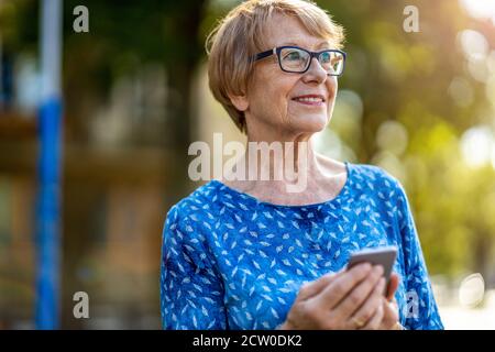 Femme âgée heureuse utilisant un téléphone mobile à l'extérieur Banque D'Images