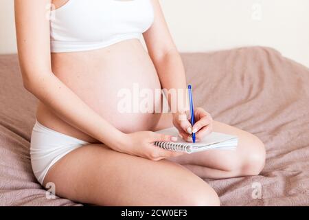 Une femme enceinte prend des notes dans un carnet. Concept de grossesse mère en attente de bébé. Banque D'Images