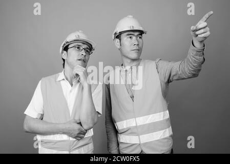 Deux jeunes hommes asiatiques ouvriers du bâtiment ensemble sur fond gris Banque D'Images