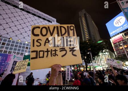 Une femme tenant un panneau de lecture, Covid-19 est un mensonge, tient un morceau de carton sur un haut-parleur pour protéger son bruit lors d'une petite manifestation ou "cluster festival" par des activistes japonais anti-masque à Hachiko Square, Shibuya, Tokyo, Japon. Samedi 26 septembre 2020.. Les militants sont partisans du controversé YouTuber devenu politicien plein d’espoir, Hiratsuka Masayuki, qui s’est présenté sans succès au gouverneur de Tokyo lors des élections du 5 juillet 2020 sous le parti libéral de souveraineté populaire. Banque D'Images