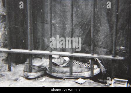 Fin années 1970 vintage noir et blanc photographie de chaussures de gym placé sur un seuil de fenêtre emprisonné. Banque D'Images