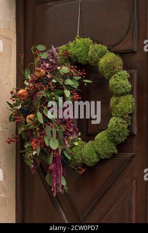 Couronne avec les baies rouges et les feuilles sèches et les fruits accrochés sur une porte. Banque D'Images