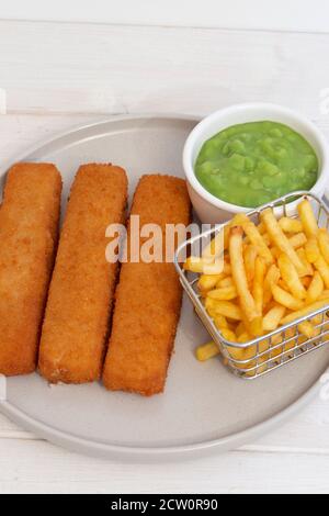 Les doigts de poisson servis avec des copeaux dans un panier en fil de fer et des pois molles. Fond en bois blanc Banque D'Images