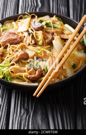 Gros plan sur les nouilles de porc et de chou sautées dans une assiette sur la table. Verticale Banque D'Images