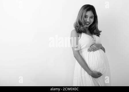 Studio shot of young happy pregnant woman smiling asiatique tout en maintenant le bébé contre le fond blanc Banque D'Images