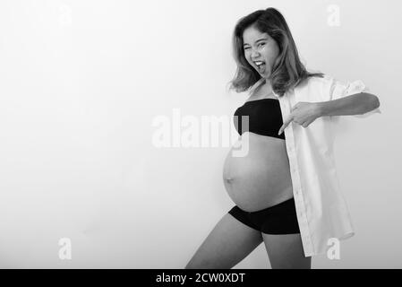 Photo en studio d'une jeune femme enceinte asiatique souriante pointant vers son estomac et en se faisant un clin d'œil Banque D'Images