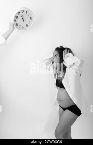 Voir le profil de jeune femme enceinte à choqué en regardant l'horloge murale against white background Banque D'Images