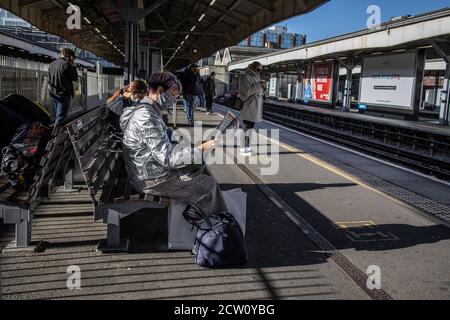Femme portant un manteau argenté imperméable lisant un journal gratuit sur la plate-forme de Wimbledon Station, sud-ouest de l'Angleterre, Royaume-Uni Banque D'Images