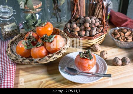 Encore la vie avec des persimmons mûrs et des paniers en osier avec des fruits secs (noix et noisettes et amandes), dans les vases de verre de fond. Banque D'Images