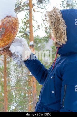 Adolescent en veste bleue dans la forêt jouant avec la neige et s'amusant. Banque D'Images