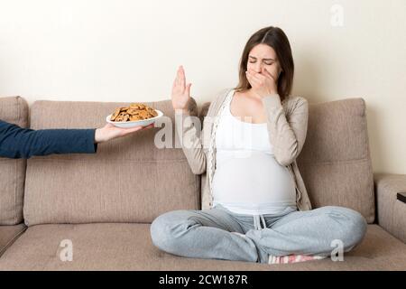 La femme enceinte assise sur le canapé refuse de manger des biscuits et ne fait aucun geste. Concept d'alimentation saine pendant la grossesse. Banque D'Images