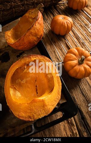 Demi-citrouilles cuites sur la plaque du four et peu de citrouilles entières brutes sur la vieille table en bois. Style rustique. Orientation verticale. Mise au point sélective. Angle élevé Banque D'Images