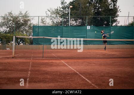 Split Croatie septembre 2020 gros plan d'un terrain de tennis orange de terre, homme de l'autre côté tournant pour frapper la balle qui vole vers le camer Banque D'Images