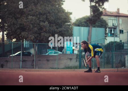 Split Croatie septembre 2020 côté d'un homme avec des cheveux plus longs jouant au tennis dehors sur un terrain d'argile orange. S'accroupir et se reposer épuisés tout en restant anti Banque D'Images