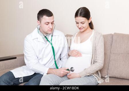 Le médecin vérifie le ventre de la femme enceinte à l'aide d'un stéthoscope. Le médecin écoute un battement de cœur d'un bébé. Banque D'Images