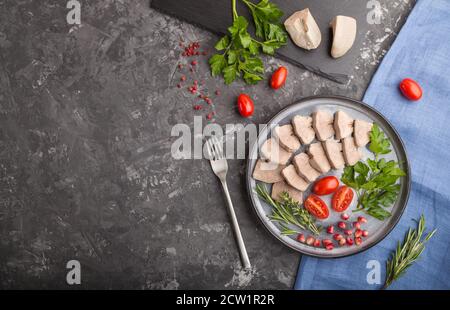 Langue de porc bouillie avec tomates et herbes sur fond de béton noir et tissu de lin bleu. Vue de dessus, espace de copie, plan de travail. Banque D'Images