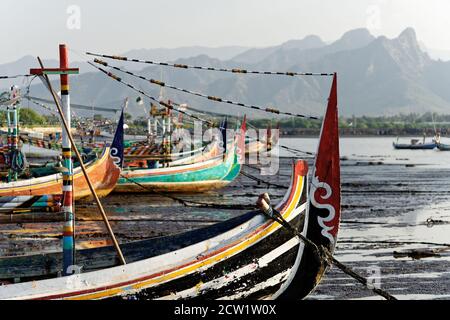 Des bateaux de pêche colorés typiques se trouvent sur la plage à marée basse, en arrière-plan une chaîne de montagnes dans la brume - emplacement: Indonésie, Java Island, Panar Banque D'Images
