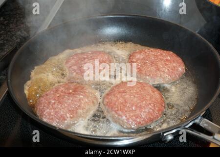 Des steaks hachés sont préparés dans une casserole sur une cuisinière à induction. Banque D'Images