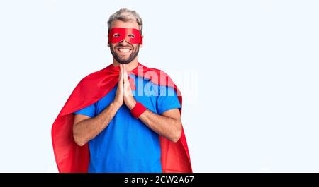 Jeune homme blond portant un super-héros crème priant avec les mains ensemble demandant pardon souriant confiant. Banque D'Images