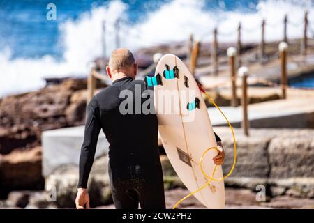 Homme australien d'âge moyen portant une combinaison de randonnée jusqu'au surf Portant sa planche de surf,Sydney,NSW,Australie Banque D'Images