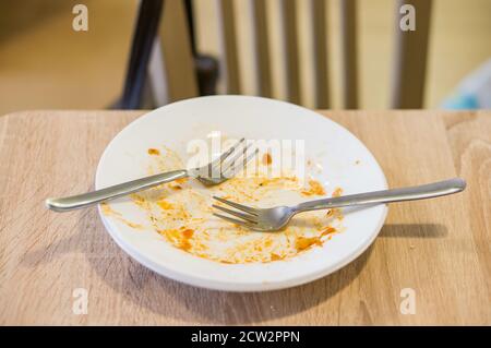 Plaque blanche avec les fourches et les restes de sauce tomate sur une table en bois en soft focus Banque D'Images