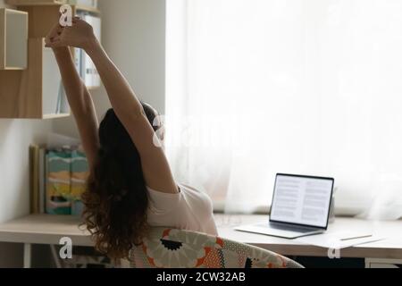 Une jeune femme s'étire sur une chaise et travaille sur un ordinateur portable Banque D'Images