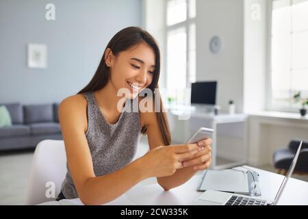 Souriant asiatique blogger fille défilant à travers les médias sociaux flux d'actualité sur téléphone portable Banque D'Images