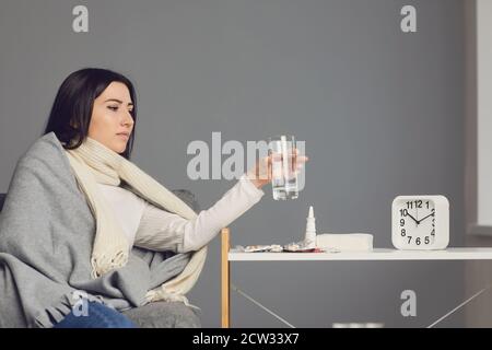 Femme dans une couverture attrapée par le froid et prenant des médicaments contre la grippe, de l'eau potable. Banque D'Images