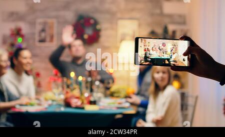 Fille prenant des photos de sa famille à l'aide d'un smartphone à la réunion de noël. Dîner de noël traditionnel en famille multigénérationnelle. Repas de Noël dans une chambre décorée. Grande réunion de famille Banque D'Images