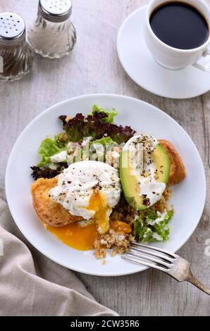 Une assiette de petit déjeuner saine et équilibrée. L'œuf de Benedict se répand sur un toast grillé avec un demi-avocat, un quinoa et une laitue, des épices assaisonnées et du yogu Banque D'Images