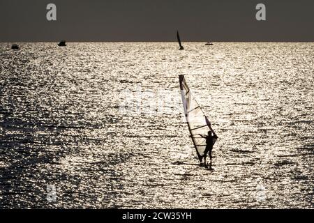 Une silhouette d'une planche à voile sur fond de coucher de soleil une surface de mer qui attrape un vent et une vague Banque D'Images