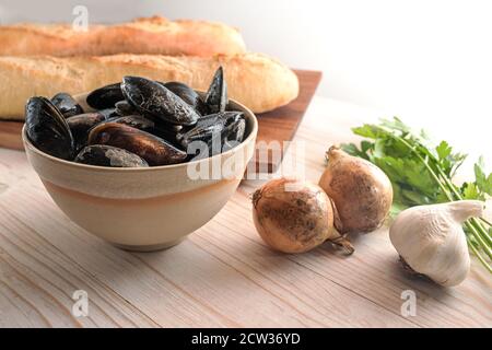 Moules et ingrédients frais crus comme l'oignon, l'ail, le persil et le pain de baguette pour un plat méditerranéen d'apéritif sur une table en bois clair, Copy spa Banque D'Images