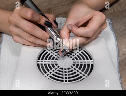 Femme enlevant shellac des ongles à l'aide d'une machine de manucure, faisant la manucure à la maison pour elle-même. Retirer le gel lustrant des ongles, les mains en gros plan. Banque D'Images